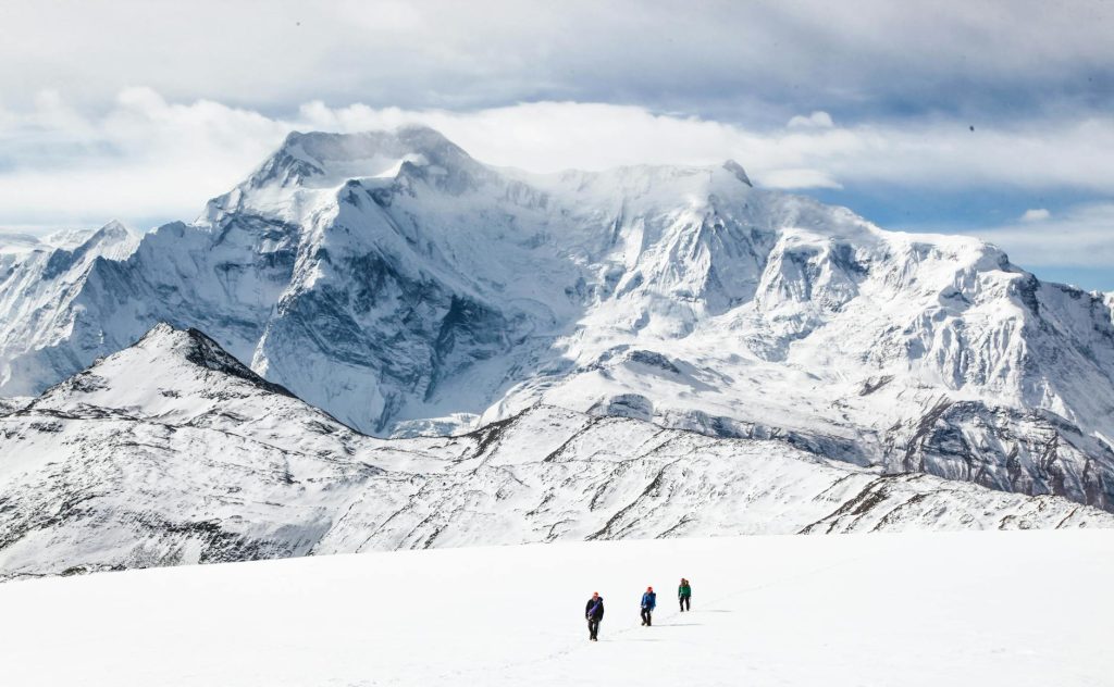 unrecognizable people walking near mountain on snowy terrain